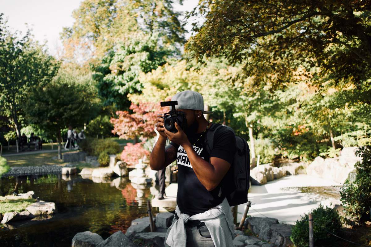 film photography man in black t-shirt and gray pants holding black dslr camera camera